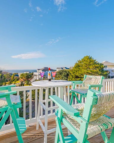 Elevated deck with green Adirondack chairs, white table, and ocean view beyond coastal homes