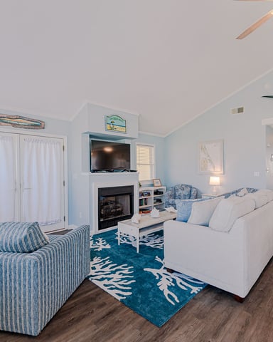 Coastal-themed living room with blue and white striped chair, cream sofa, fireplace with TV, and marlin sculpture on ceiling