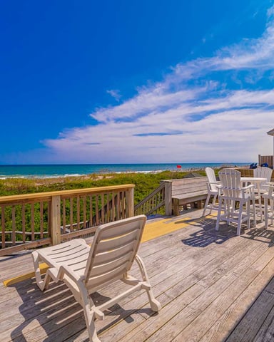 Oceanfront deck with lounge chairs, dining table, and beach views under clear blue sky