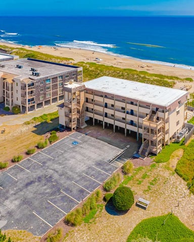 Aerial view of beachfront vacation rental buildings with sandy beach, ocean, and dune vegetation
