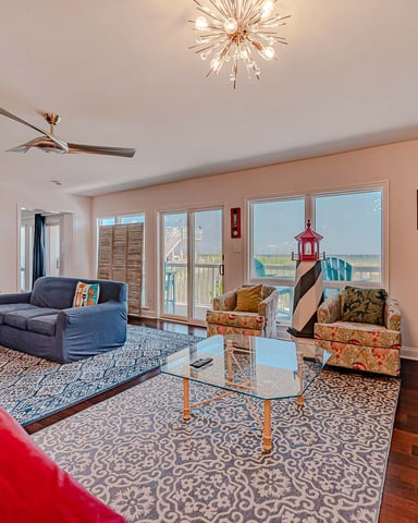 Spacious living room with ocean and lighthouse views, blue sofa, patterned armchairs, glass coffee table, and coastal décor.