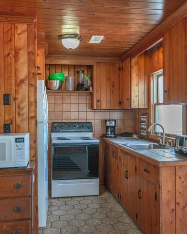 Rustic wood-paneled kitchen with stove, refrigerator, microwave, and tile countertops