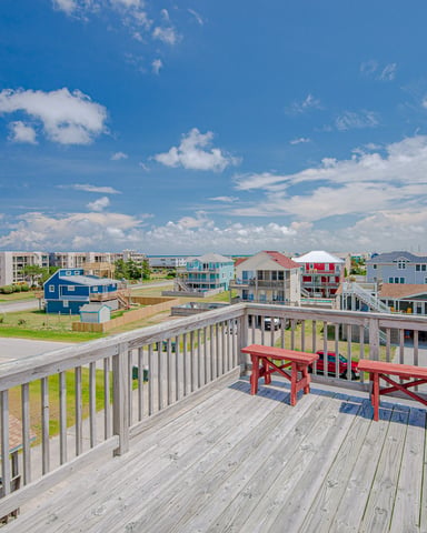 Wooden deck with red benches overlooking colorful beach houses and ocean under blue sky