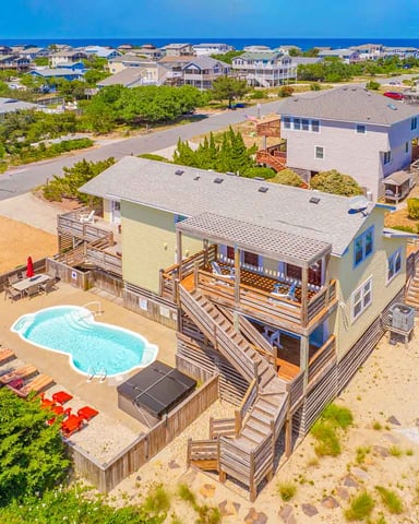 Aerial view of beachfront house with pool, wooden deck, and ocean view in residential coastal community