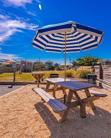 Beachside patio with striped umbrella, picnic table, wooden fence, and residential neighborhood under clear blue sky