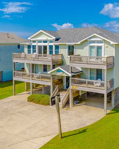 Elevated beach houses with decks and pilings on grassy lot under blue sky