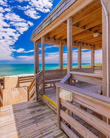 Wooden beach pavilion with ocean view, sandy beach, dune grass, and blue sky with clouds
