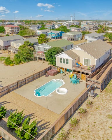 Aerial view of beachfront house with pool, playground, and deck overlooking sandy beach and neighboring homes