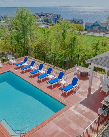 Waterfront pool deck with lounge chairs, pergola, and gazebo overlooking bay and residential homes