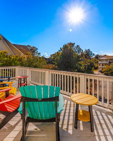 Sunny deck with colorful Adirondack chairs overlooking forested neighborhood and distant houses