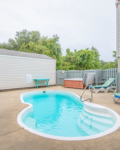 Backyard pool area with turquoise lounge chairs, umbrella, hot tub, and white-railed deck attached to house