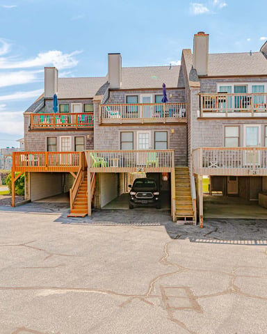 Beachfront vacation rental homes with elevated decks, wooden railings, and ground-level garages on sandy beach