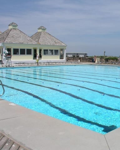 Olympic-size swimming pool with lane dividers and pale yellow pavilion building with domed roof