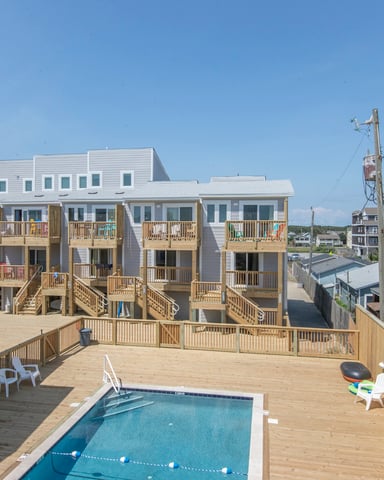 Beachfront multi-unit vacation rental with white siding, wooden decks, and pool surrounded by coastal homes