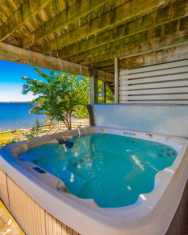 Hot tub on wooden deck with ocean and blue sky view, covered by wooden pergola