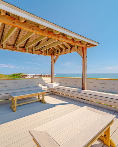 Wooden pergola with built-in benches on oceanfront deck overlooking beach and calm blue water