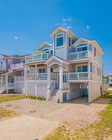 Beachfront vacation rental with white siding, multiple decks, and blue trim under clear sky