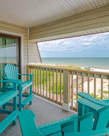 Beachfront deck with turquoise Adirondack chairs overlooking sandy beach and ocean horizon