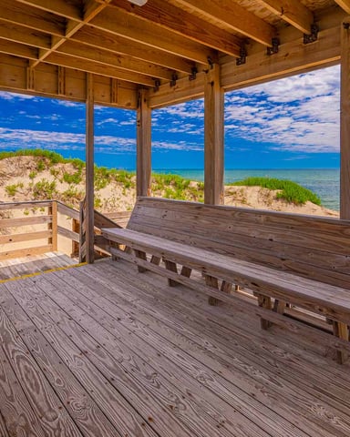 Wooden beach pavilion with benches overlooking sand dunes, ocean, and blue sky