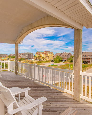 Covered deck with white Adirondack chairs overlooking beach houses and ocean in coastal neighborhood