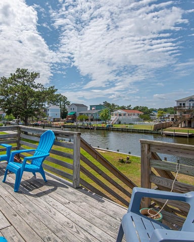 Waterfront deck with blue Adirondack chairs overlooking canal, residential homes, and docked boats