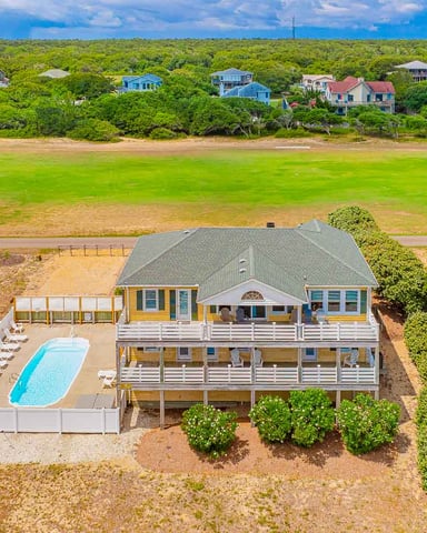 Elevated beach house with pool, multiple decks, and ocean view across sandy dunes and marsh.