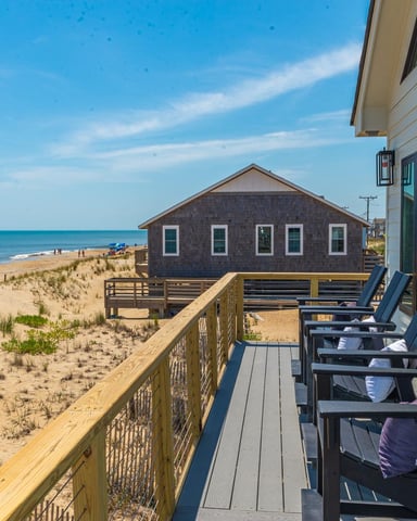 Oceanfront deck with Adirondack chairs overlooking sandy beach, dunes, and neighboring beach house