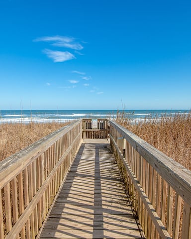 Wooden boardwalk through beach dunes with ocean and blue sky beyond