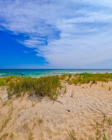 Sandy beach with dune grass, turquoise ocean, and blue sky with wispy clouds