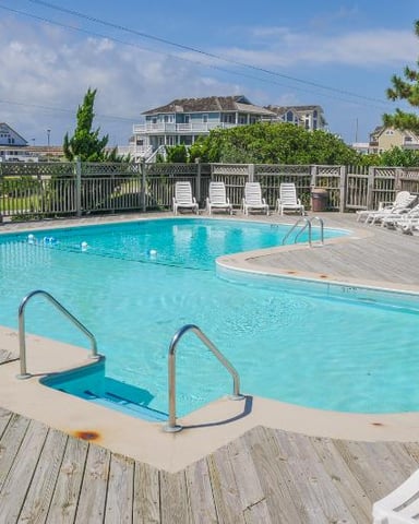Community swimming pool with lounge chairs, wooden deck, and residential houses in background