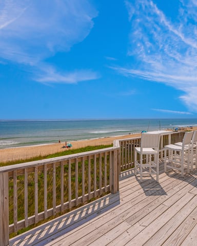 Oceanfront deck with white railings and bar seating overlooking sandy beach and blue ocean