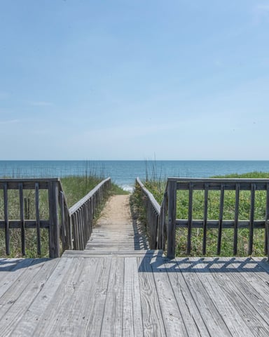 Wooden beach deck with railings and boardwalk leading to ocean and dunes with beach grass