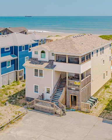 Aerial view of beachfront vacation rental homes with sandy dunes, ocean, and a distant boat on the horizon