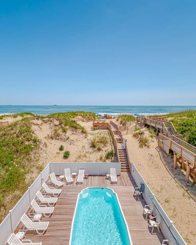 Oceanfront vacation home with swimming pool, wooden deck, beach access stairs, and sand dunes with beach grass