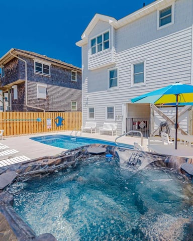 Beachfront house with hot tub, swimming pool, lounge chairs, and colorful umbrellas in fenced yard