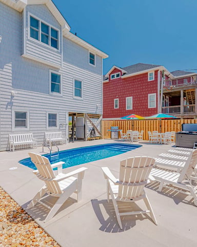 Beachfront vacation rental with swimming pool, lounge chairs, and two elevated houses with white and red siding