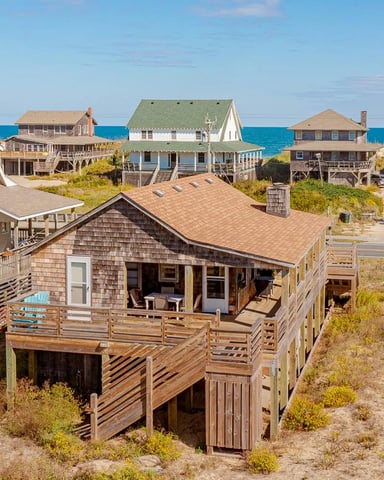 Beachfront vacation homes with wooden decks and pilings along sandy shore and ocean view
