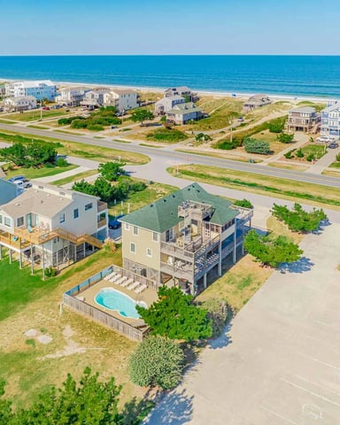 Aerial view of beachfront vacation homes with swimming pool, dunes, and ocean beyond