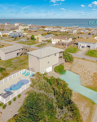 Aerial view of beachfront neighborhood with houses, pools, and tidal waterway leading to ocean