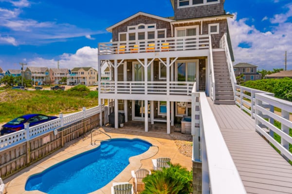 Elevated beach house with white railings, blue pool, and wooden deck overlooking coastal neighborhood