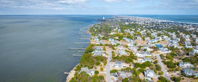 Aerial view of coastal residential community with waterfront homes, docks, and tree-lined streets along bay