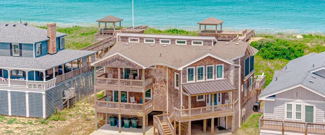 Beachfront vacation homes with elevated decks overlooking turquoise ocean and sandy beach with gazebos